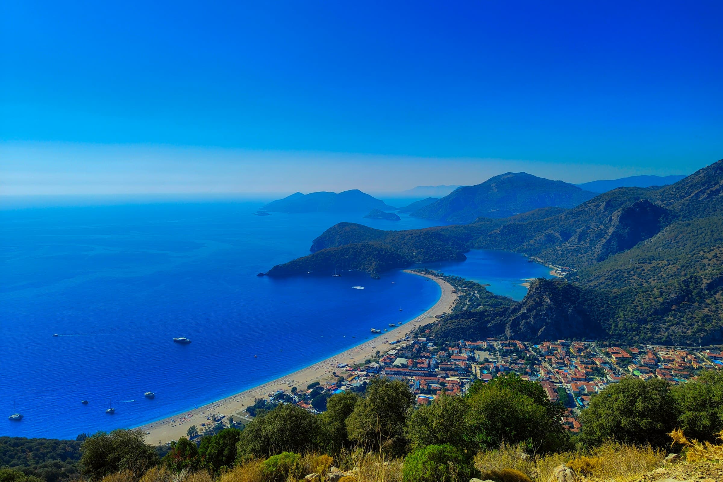Looking down from coastal mountains onto a deep-blue sea and a curving beach
