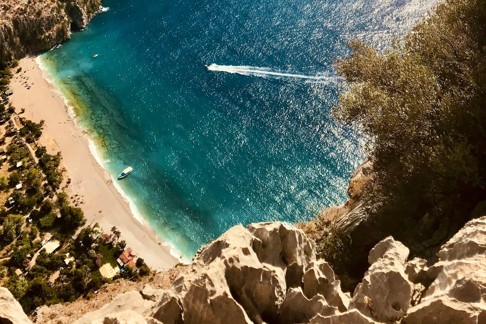 A cove between sheer cliffs, turquoise water and a boat's wake