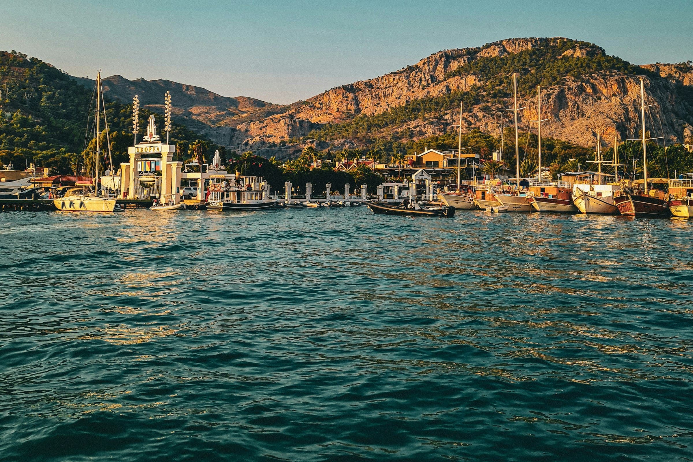 Akşam ışığında tekne dolu liman, arkada dağlar